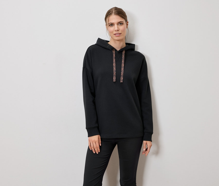 Žena má na sobě černou mikinu s kapucí a kalhoty.