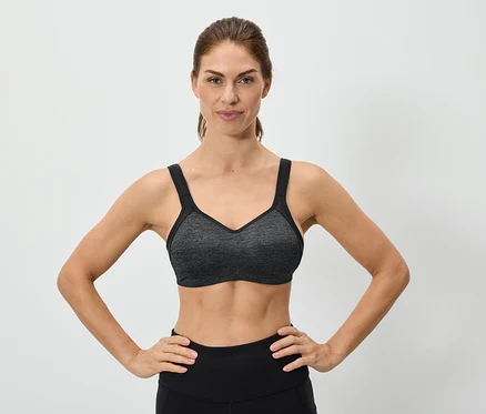 Žena s rukama na bocích má na sobě šedou sportovní podprsenku.