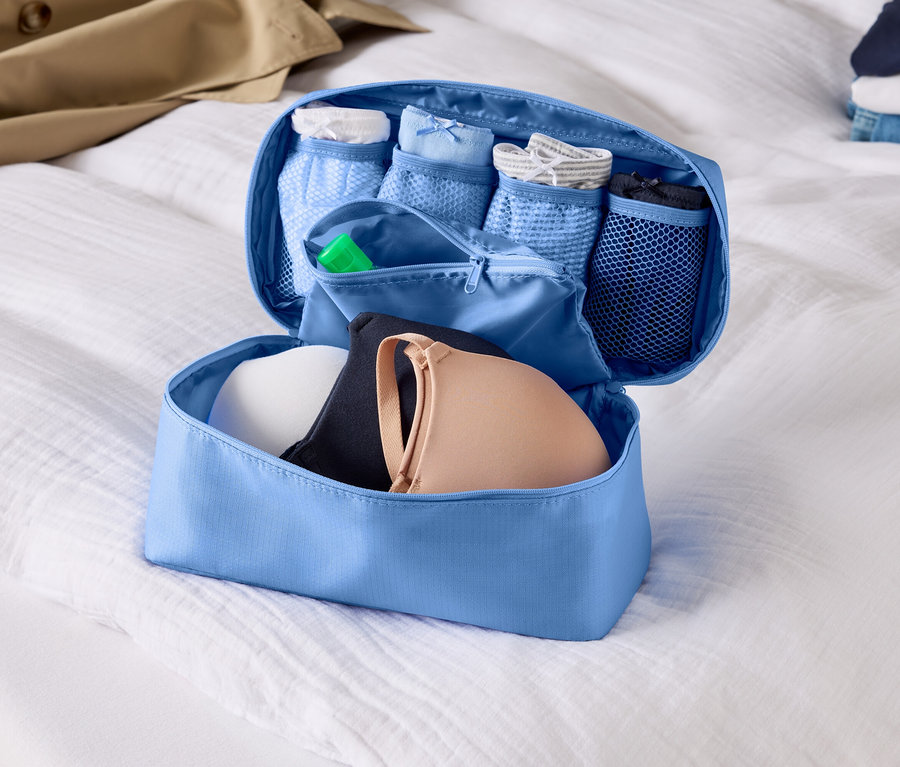 Otevřený, světle modrý organizér zavazadel s podprsenkami a spodním prádlem na bílém prostěradle.