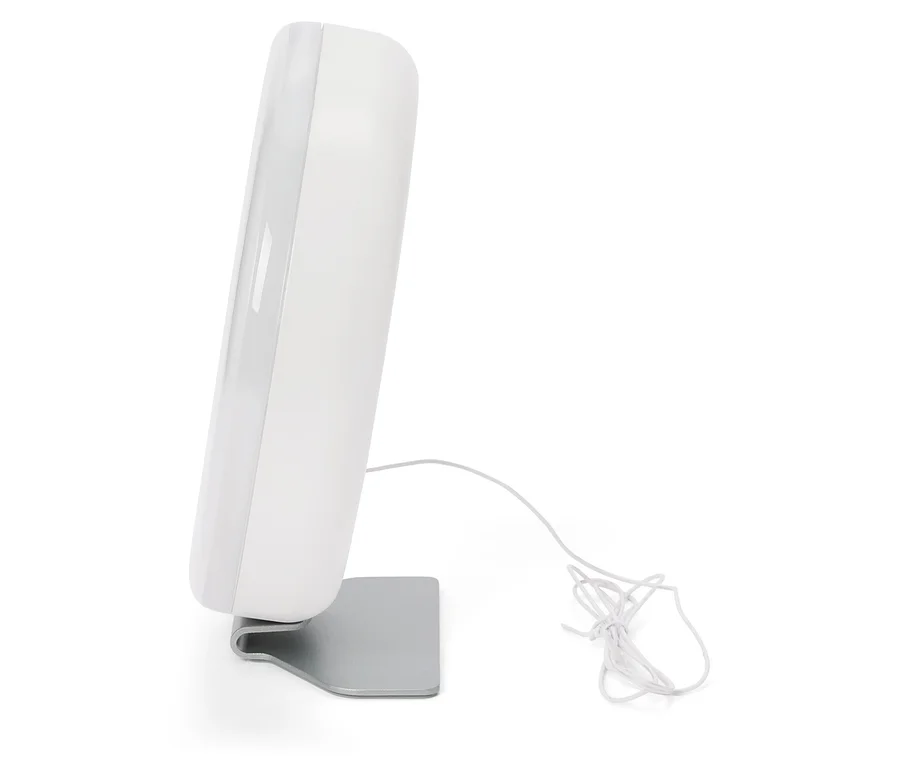 Bílá lampa pro světelnou terapii stojí na stříbrném stojanu, kabel leží vedle ní.