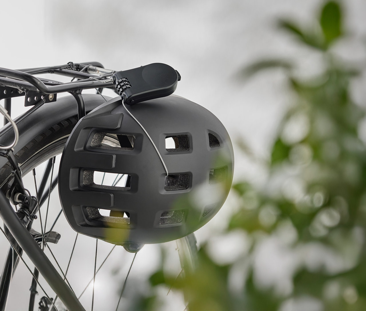 Černá cyklistická helma visí se zámkem na nosiči kola.