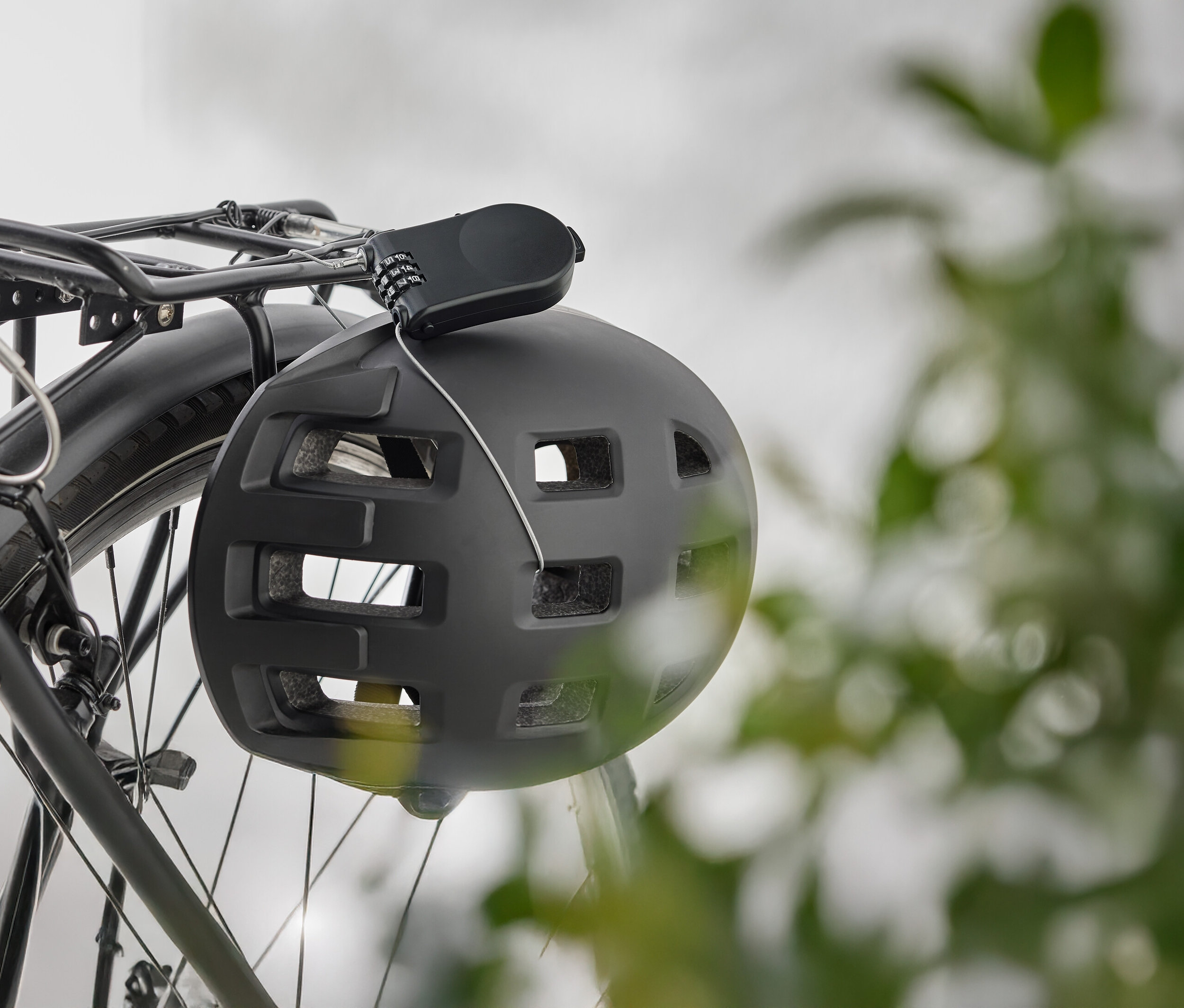 Černá cyklistická helma visí se zámkem na nosiči kola.