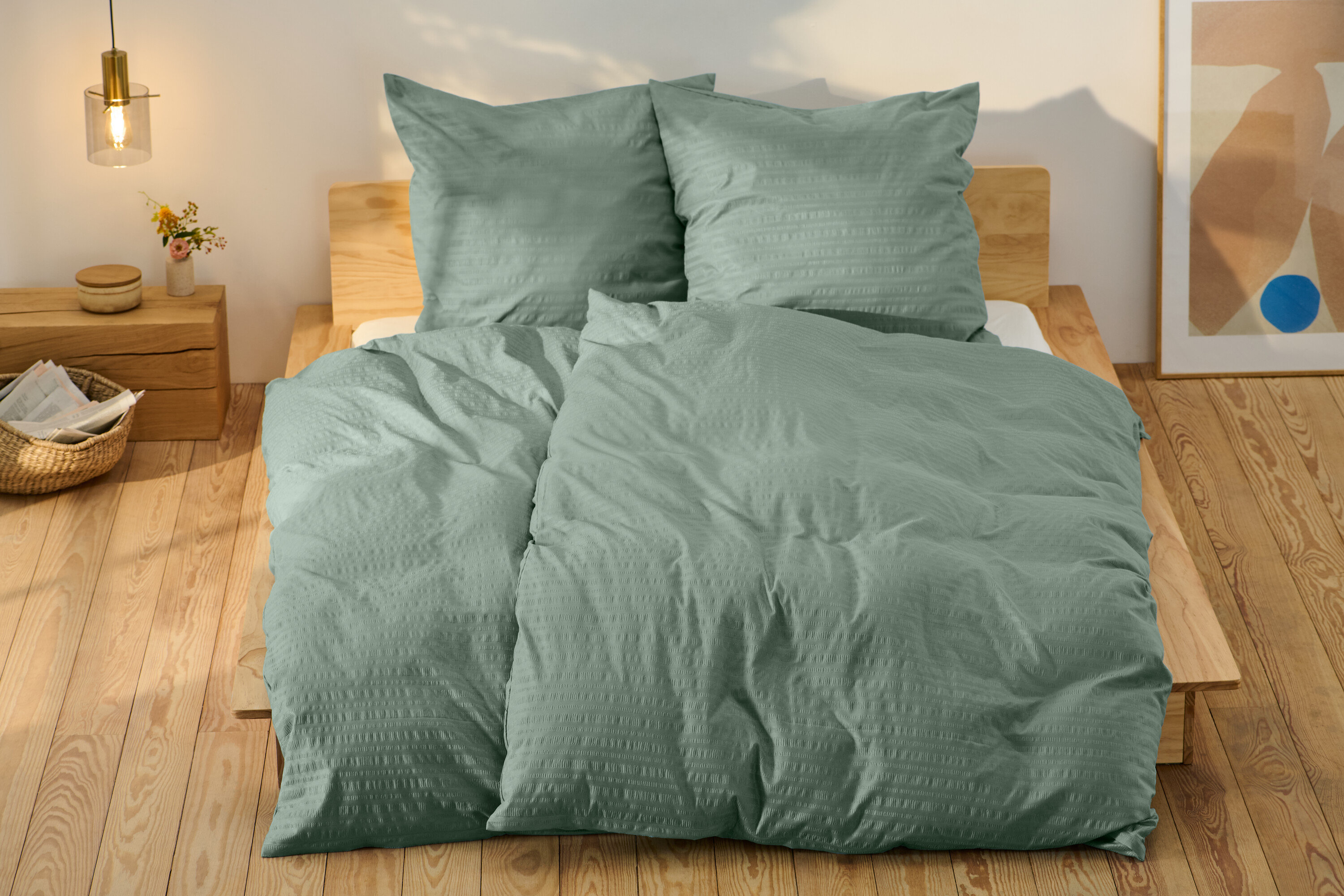 Zelené krepové povlečení standardní velikosti a jedno nadměrné velikosti na posteli.