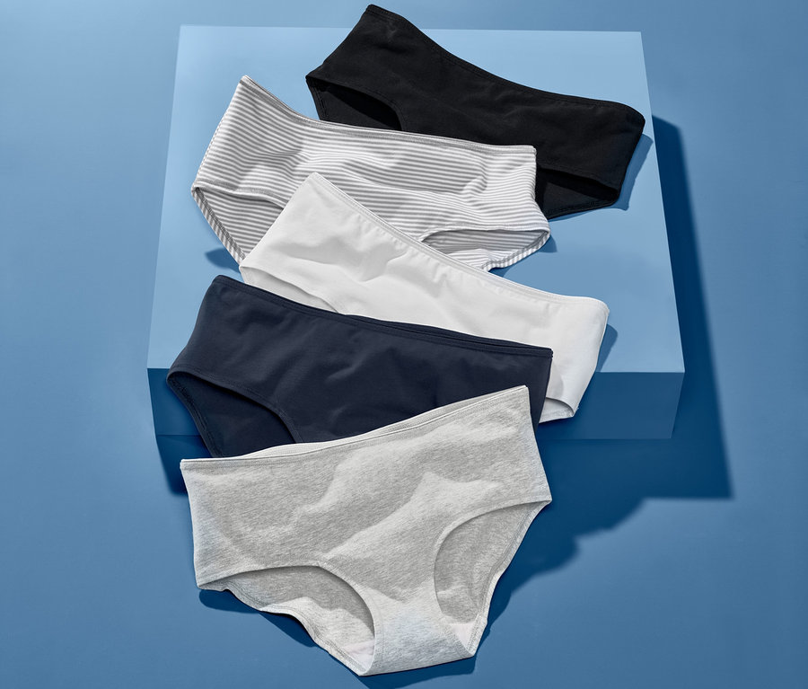 Pětice kalhotek různých barev leží na modrém pozadí. V balení jsou černé, proužkované, bílé, tmavě modré a šedé kalhotky.