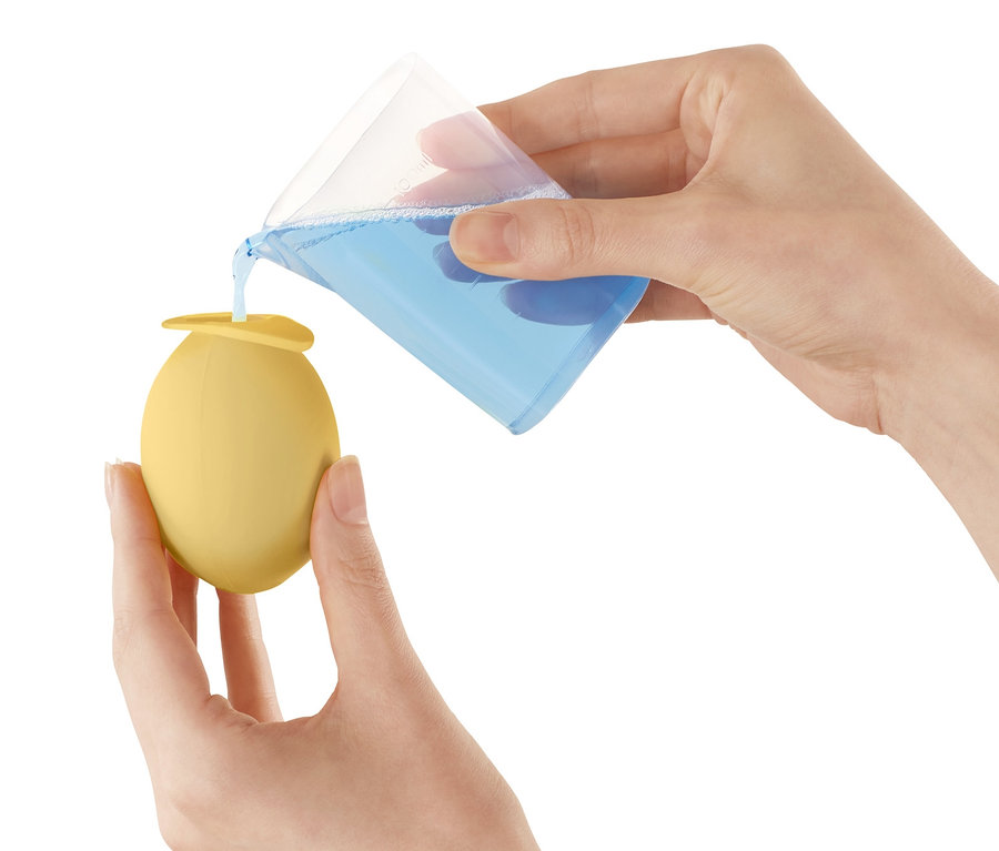 Osoba nalévá modrou tekutinu z odměrky do žlutého nástavce na odvápnění vodovodního kohoutku.