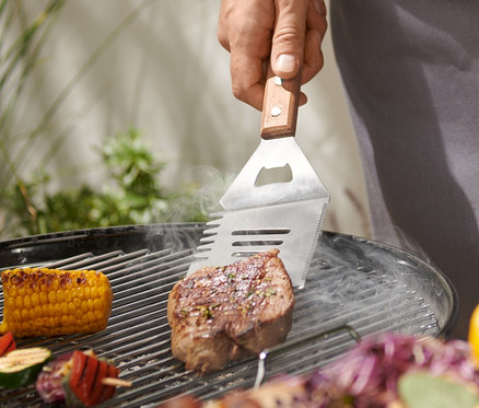 Muž griluje steak pomocí multifunkčního BBQ náčiní.