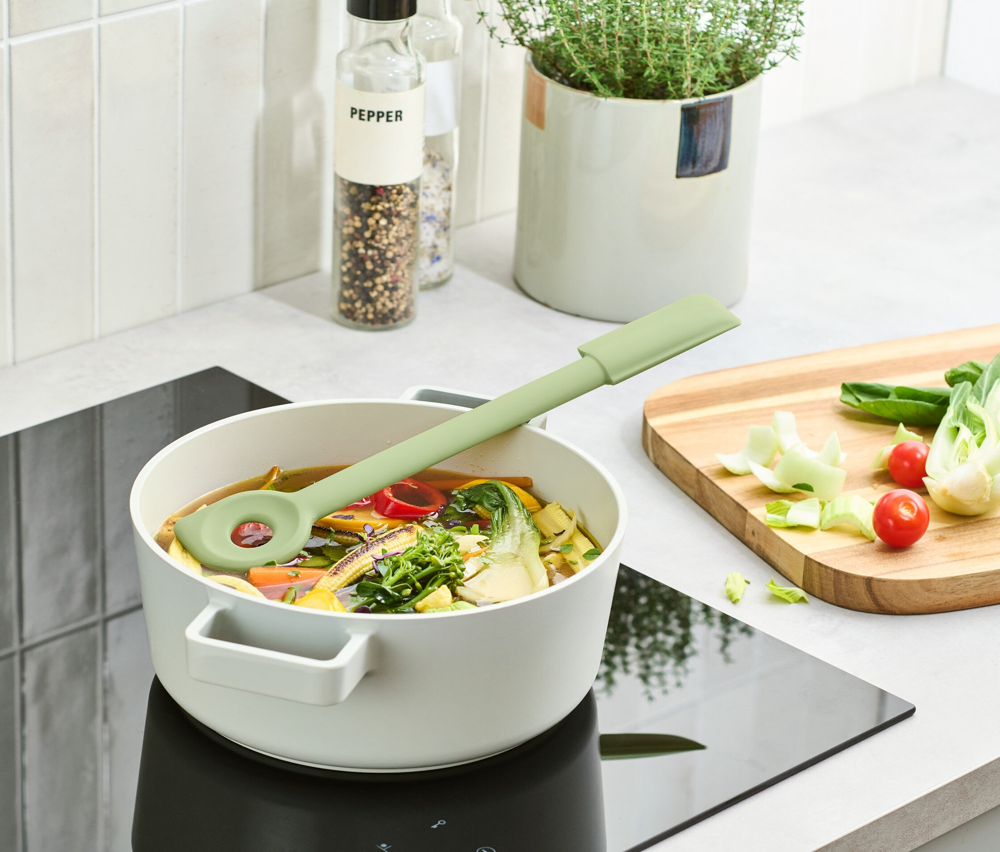 Zelená multifunkční vařečka leží v hrnci s polévkou na indukční varné desce.