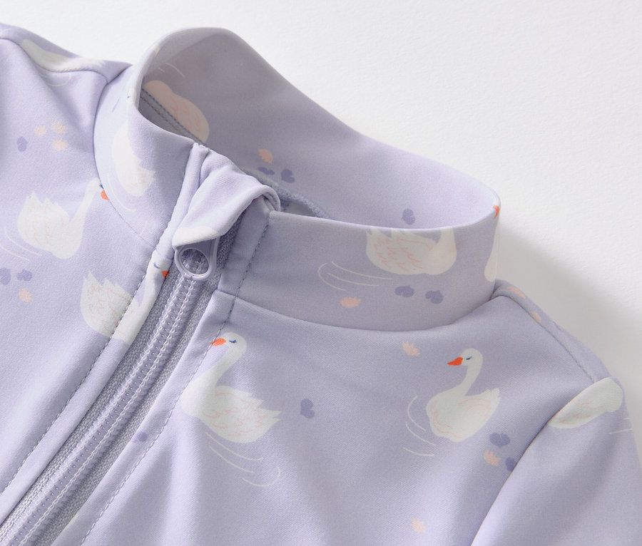 Detail fialového overalu s potiskem labutí a zipem, s UV faktorem 80 pro miminka.