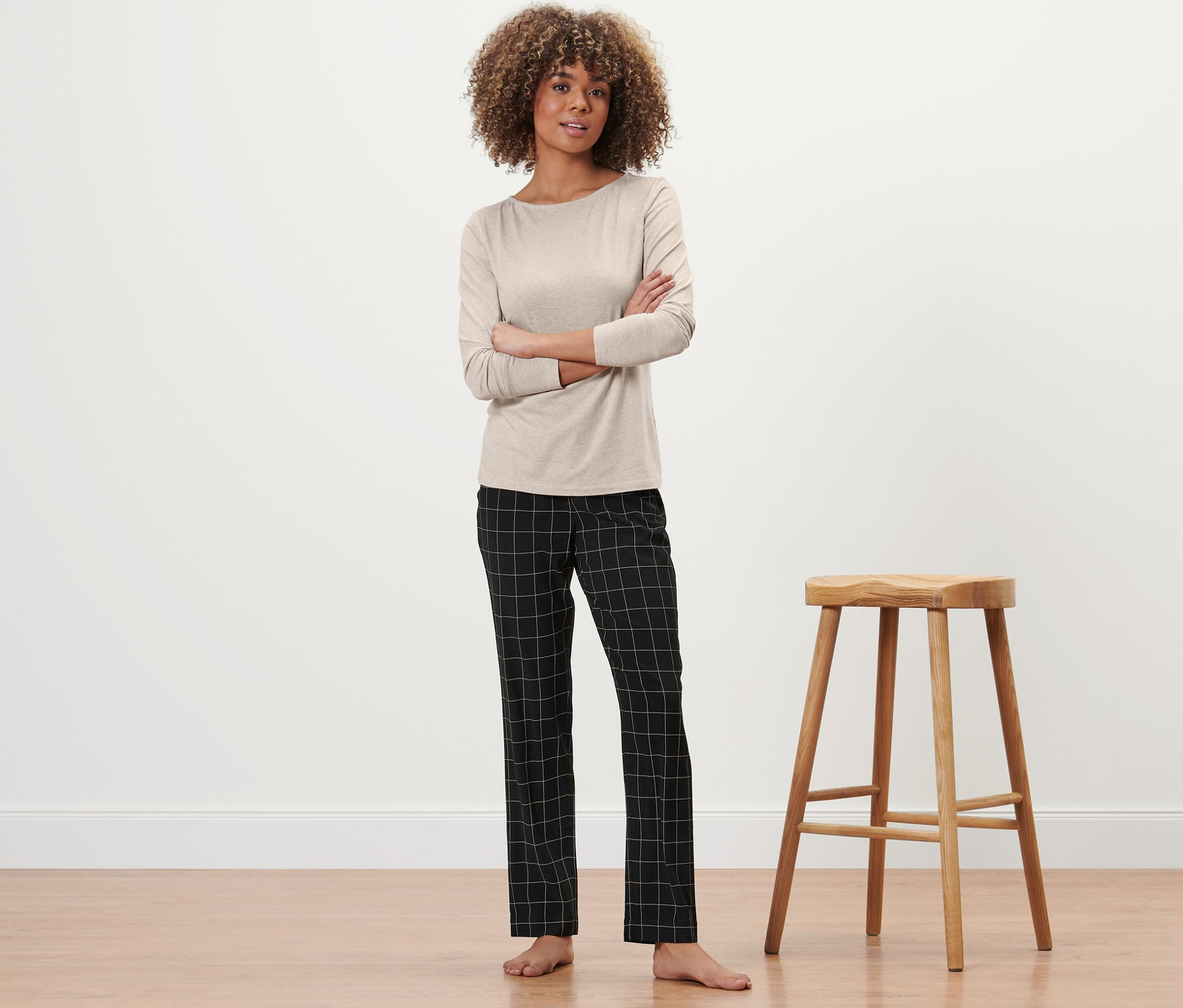 Žena pózuje v pyžamu vedle dřevěné stoličky.