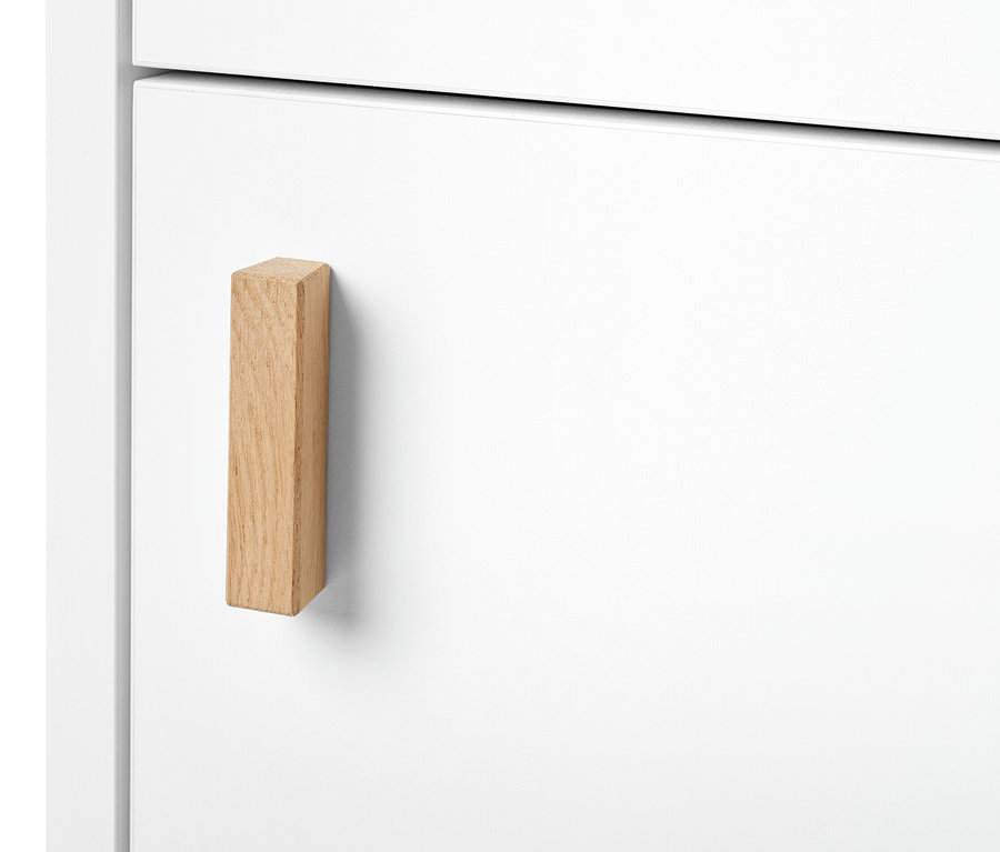 Detail úzké koupelnové skříňky s dvířky a dřevěnou rukojetí.