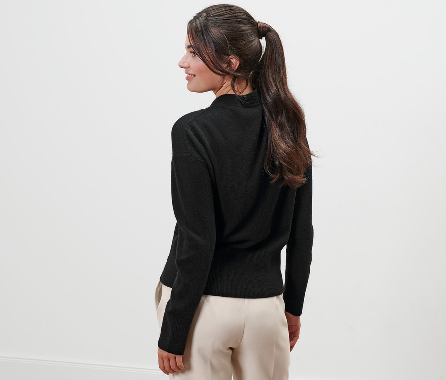 Žena se dívá přes rameno a má na sobě černý svetr z jemného úpletu s kašmírem.