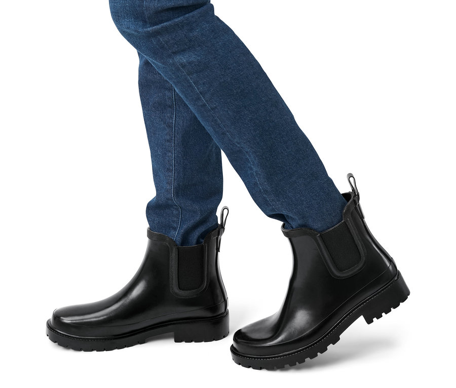 Nohy osoby v džínách a nízkých holínkách.