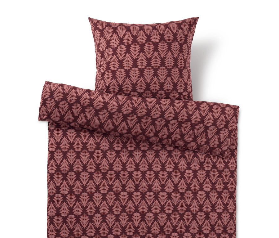 Povlečení a polštář s listovým vzorem v odstínech červené.