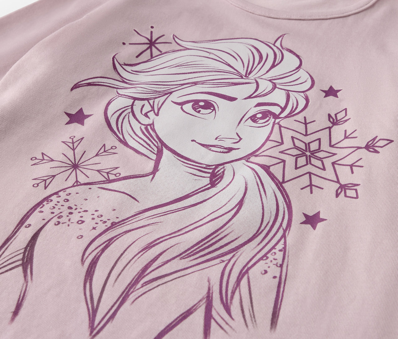 Detail dětského pyžamového setu »Ledová princezna« s kreslenou Elsou, vločkami a hvězdami na růžovém tričku.