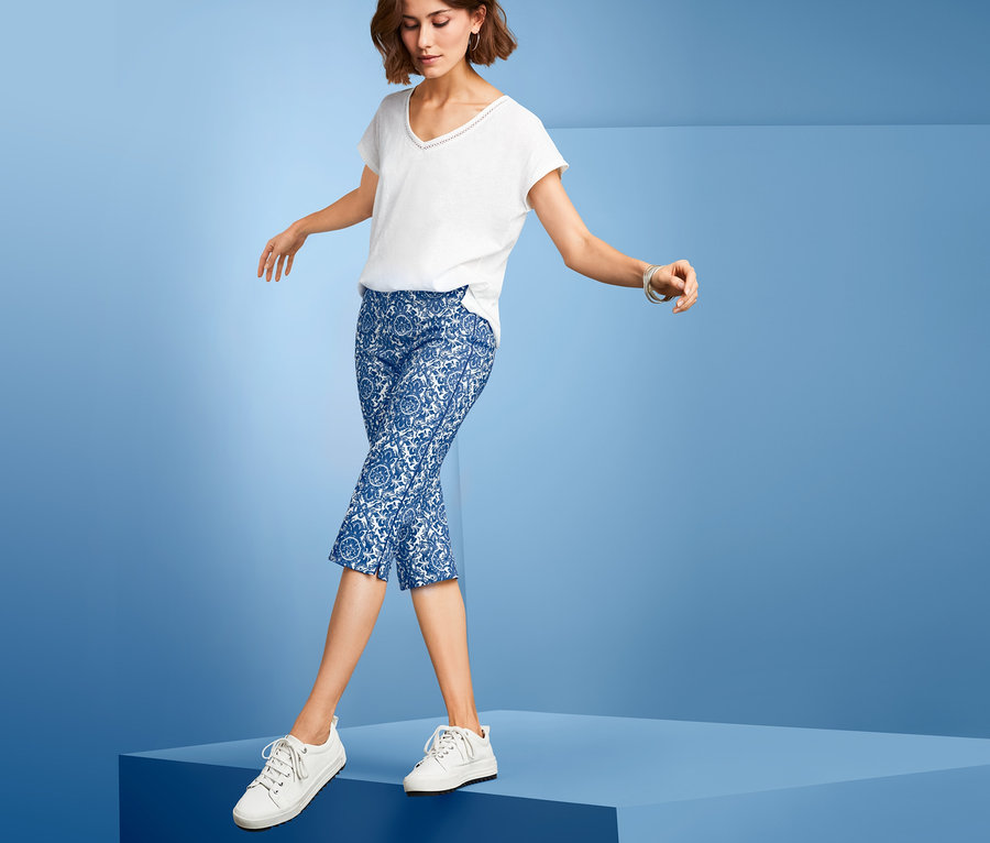 Žena kráčí po modré plošině a má na sobě modré 3/4 strečové kalhoty s potiskem.