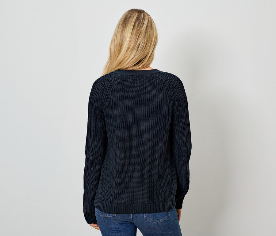 Žena zády k fotoaparátu má na sobě tmavě modrý svetr a džíny.