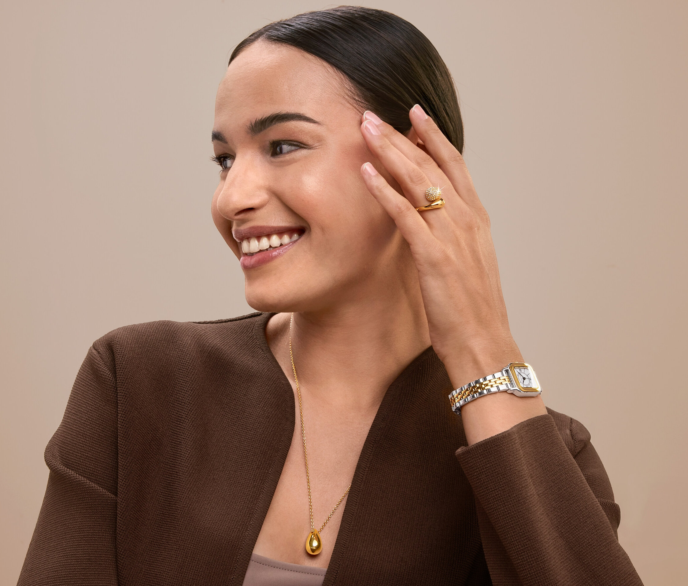 Usmívající se žena se dotýká tváře, má na sobě zlatý prsten, hodinky a náhrdelník.