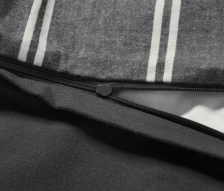 Detail šedého povlečení s bílými pruhy a černým zipem.