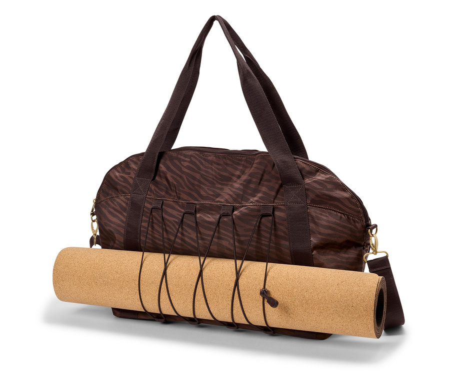 Hnědá sportovní taška se zebřím potiskem drží srolovanou korkovou podložku na jógu.