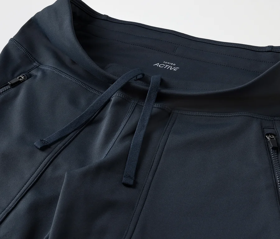 Detailní záběr na tmavě modré sportovní kalhoty s kapsami na zip a stahovací šňůrkou.