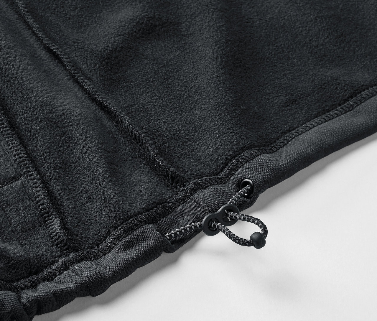 Detail černého fleecového svetru se stahovací šňůrkou.