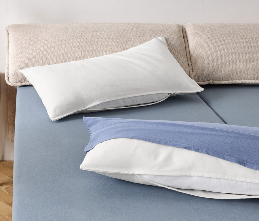 Dva bílé polštáře a jeden bílý polštář s modrým povlakem na modré posteli.