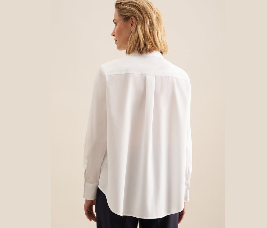 Zezadu je vidět žena v bílé nežehlivé halence Seidensticker.