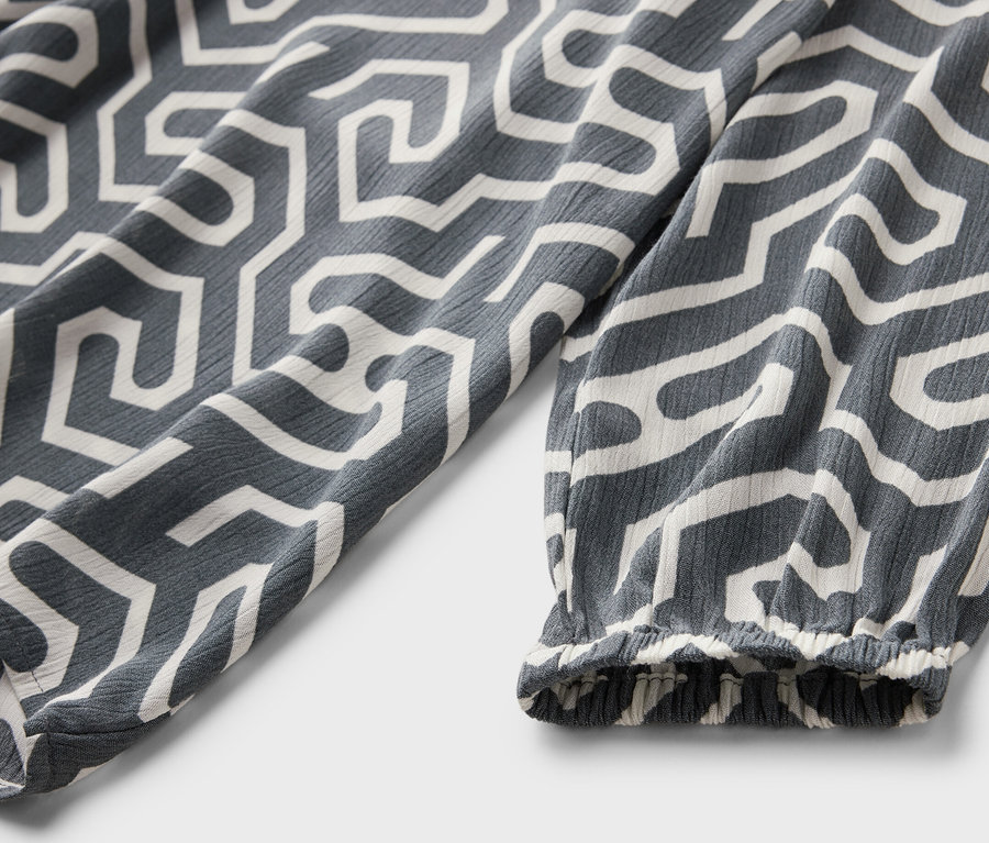 Detail šedé halenky v mačkaném vzhledu s bílým geometrickým vzorem.