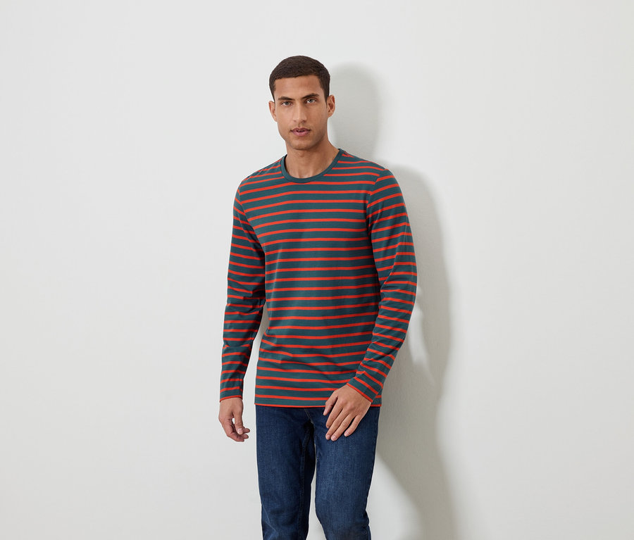 Muž stojí a má na sobě pruhované tričko s dlouhým rukávem a džíny.