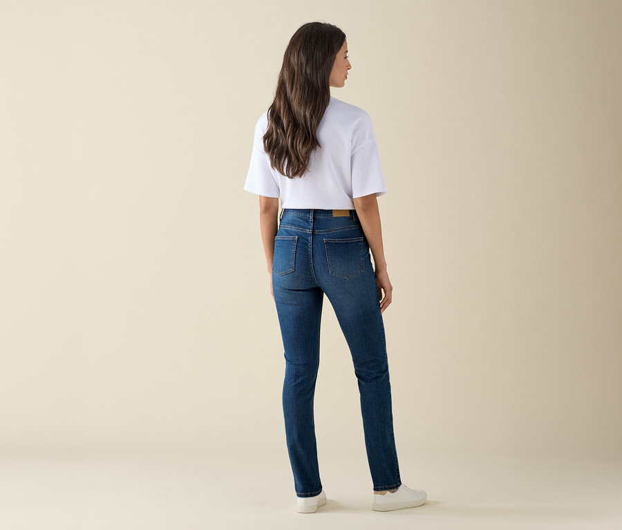 Žena stojí zády a má na sobě džíny slim střihu »Emma«, mid blue denim, bílé tričko a tenisky.