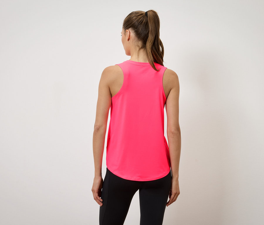 Žena v růžovém tílku a černých legínách stojí zády ke kameře.