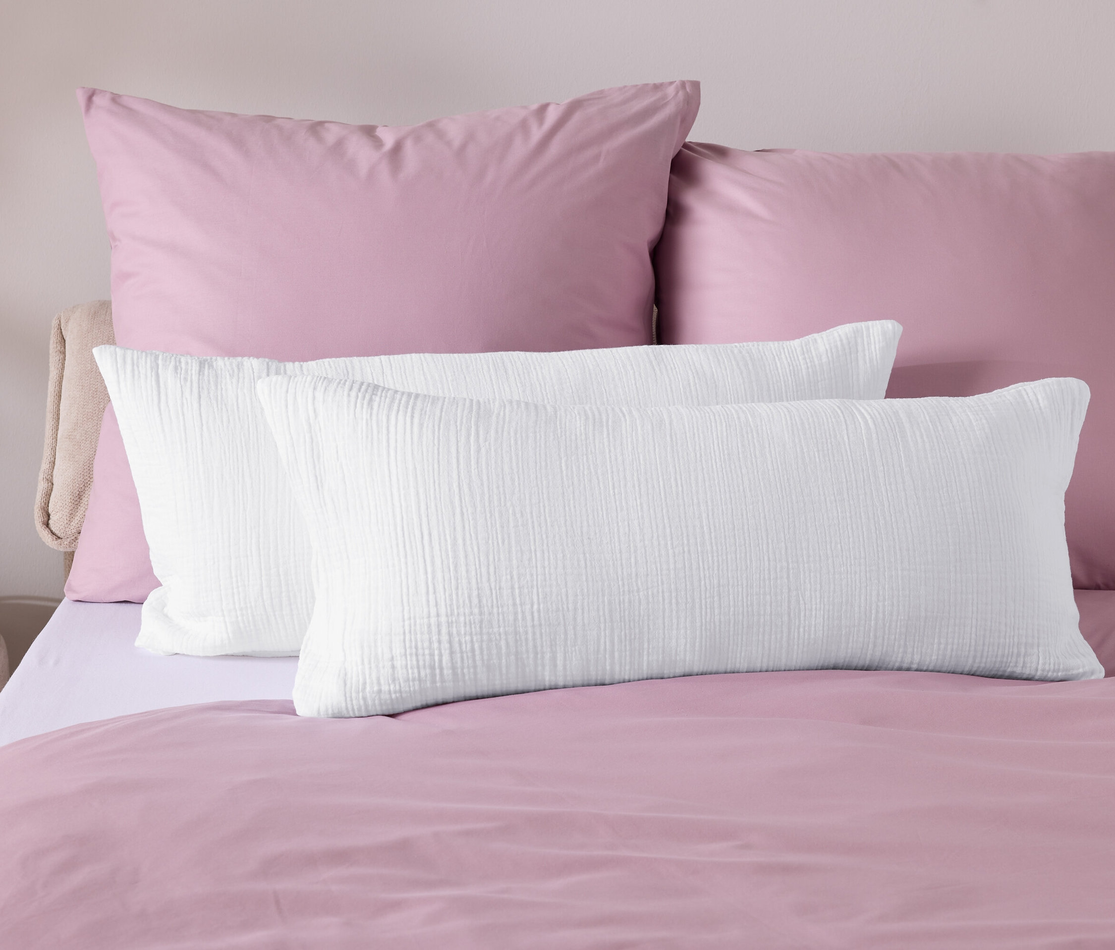 Detail ložního prádla s růžovým povlečením a bílými polštáři.