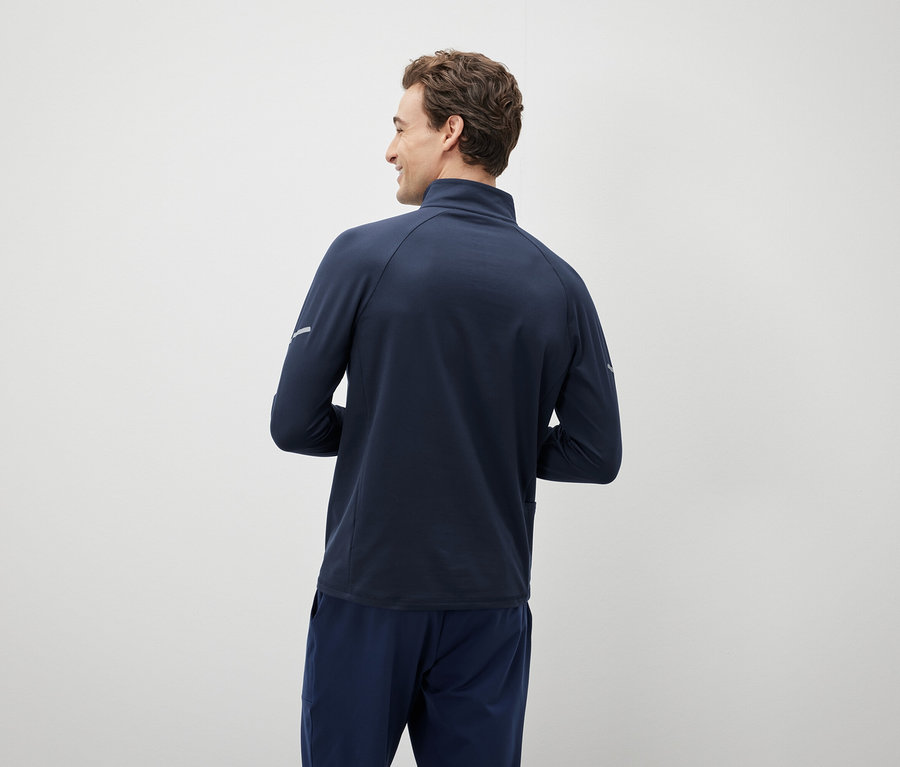 Muž se dívá přes rameno a má na sobě tmavě modrou bundu a kalhoty.