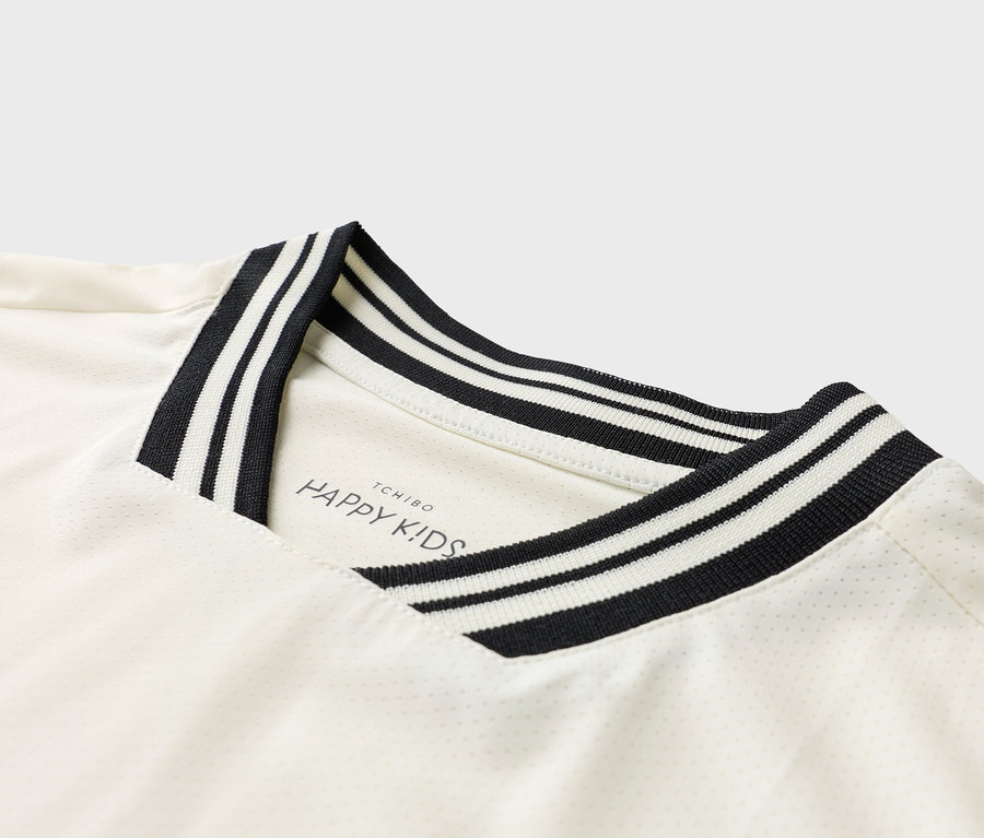 Detailní pohled na bílé tričko s černo-bílým pruhovaným límcem a logem 'TCHIBO HAPPY KIDS'.