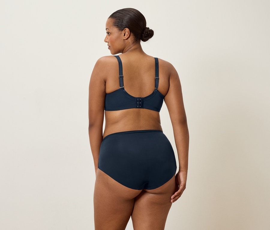 Žena s tmavými vlasy, viděná zezadu, má na sobě tmavě modrou podprsenku a odpovídající kalhotky.