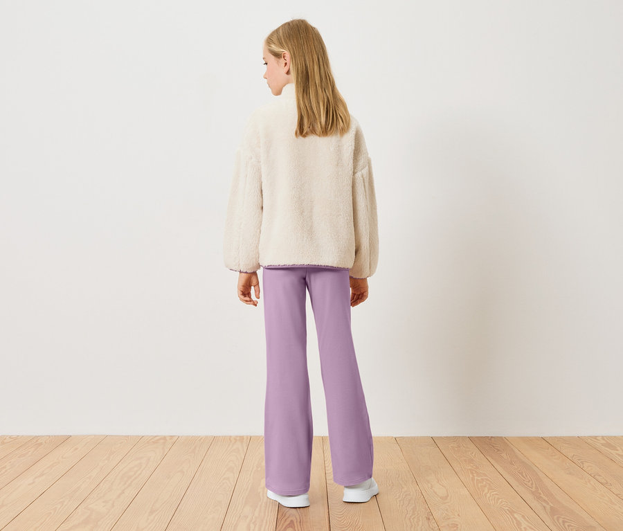Pohled zezadu na blondýnu v krémovém teddy fleecovém topu a fialových kalhotách.