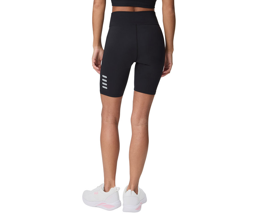 Žena zezadu v černých cyklistických šortkách se čtyřmi reflexními pruhy a bílých teniskách.