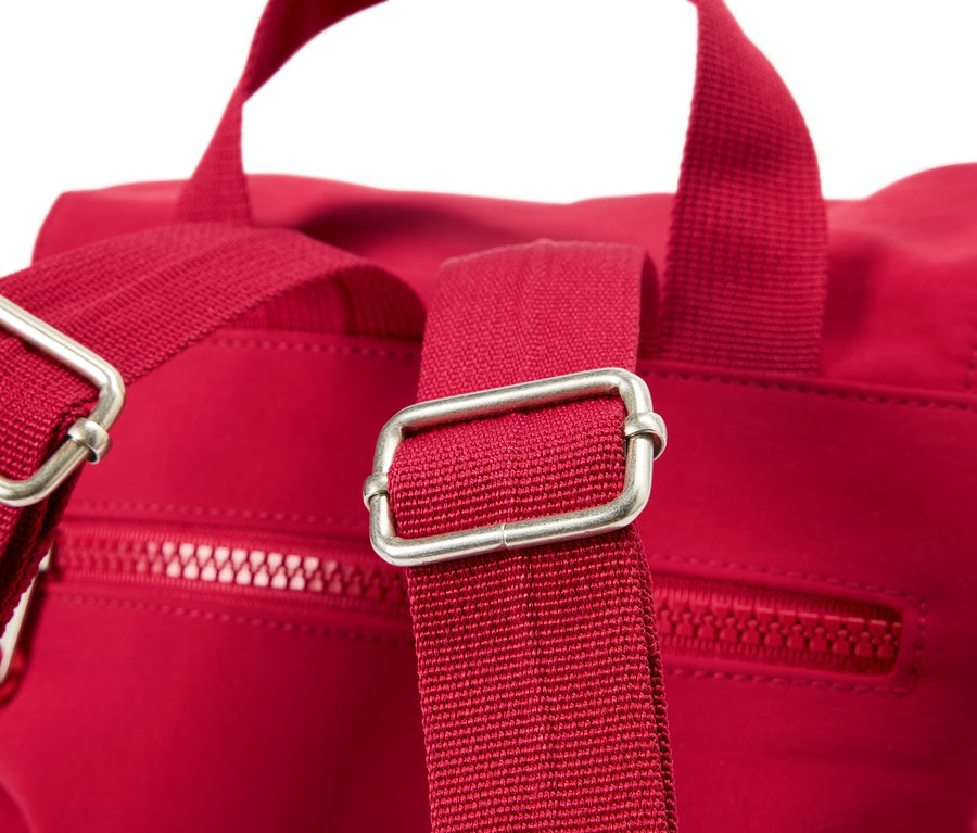 Detailní záběr na červený batoh se stříbrnými přezkami na popruzích.