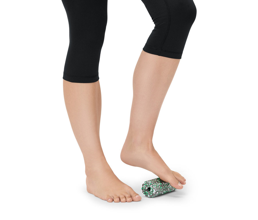 Žena v černých legínách válí nohu na zeleno-bílém pěnovém válci.