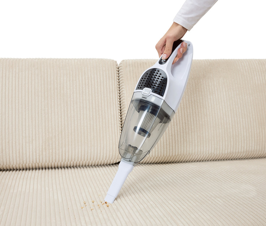 Ruka vysává drobky z béžové pohovky pomocí akumulátorového vysavače 2 v 1.