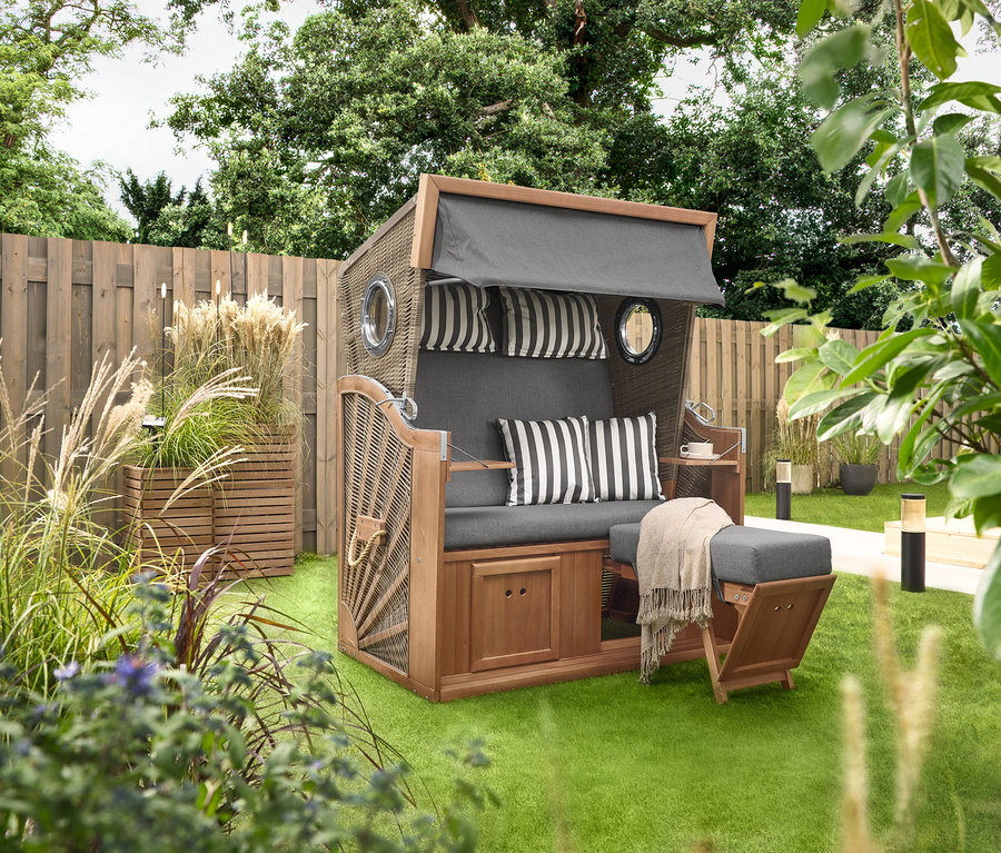 Na trávě stojí plážový koš Premium XL se 2 výklopnými stolky, vedle něj 2 truhlíky »Tinus«. V pozadí jsou vidět solární zápichy s LED, 5 ks.