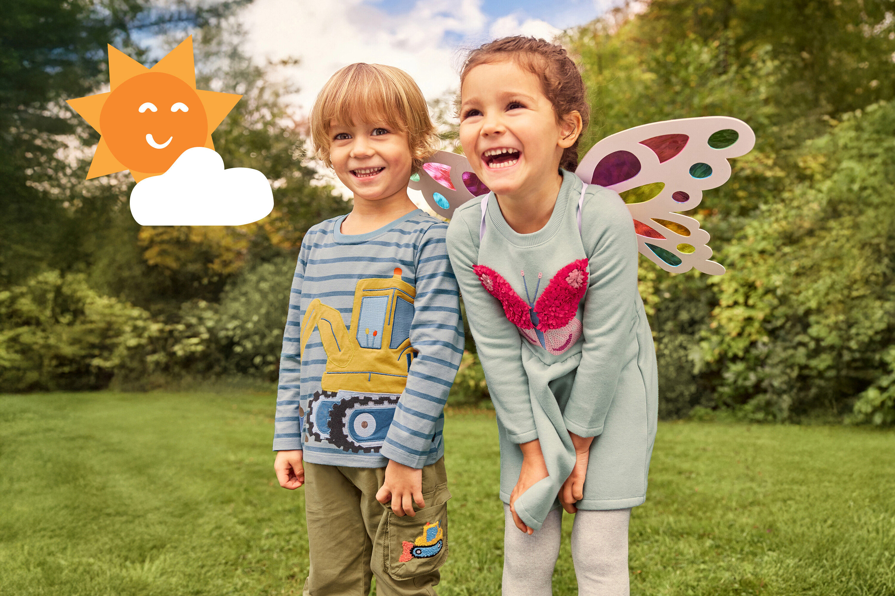 Dvě smějící se děti stojí v trávě. Dívka má na sobě křídla a šaty s motýlem, chlapec má tričko s bagrem.