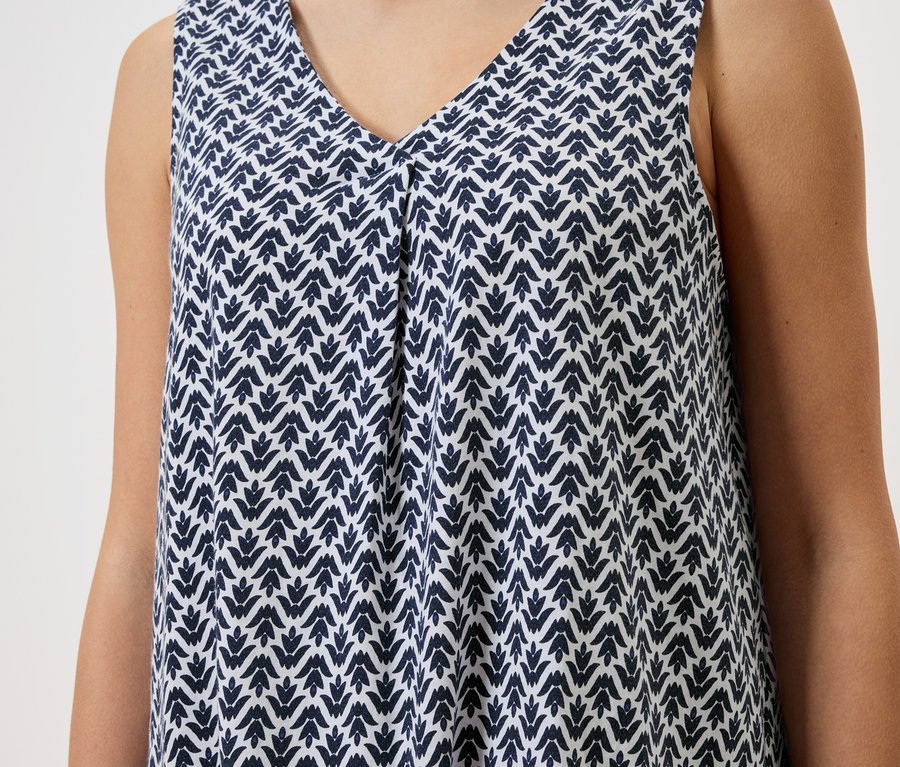 Detailní záběr ženy v šatech bez rukávů s modrobílým vzorem.