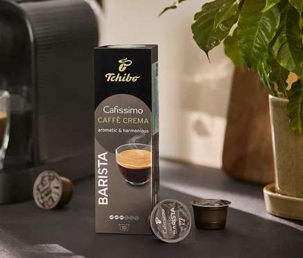 Kávovar plní sklenici kávou. Vedle stojí balení Cafissimo BARISTA Caffè Crema a několik kapslí.