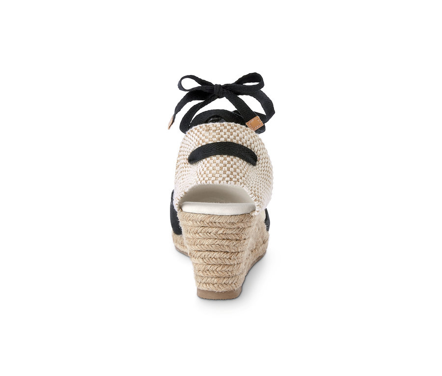 Detail zadní strany espadrilky s klínovým podpatkem, která má černou stuhu a béžovou pletenou patu.