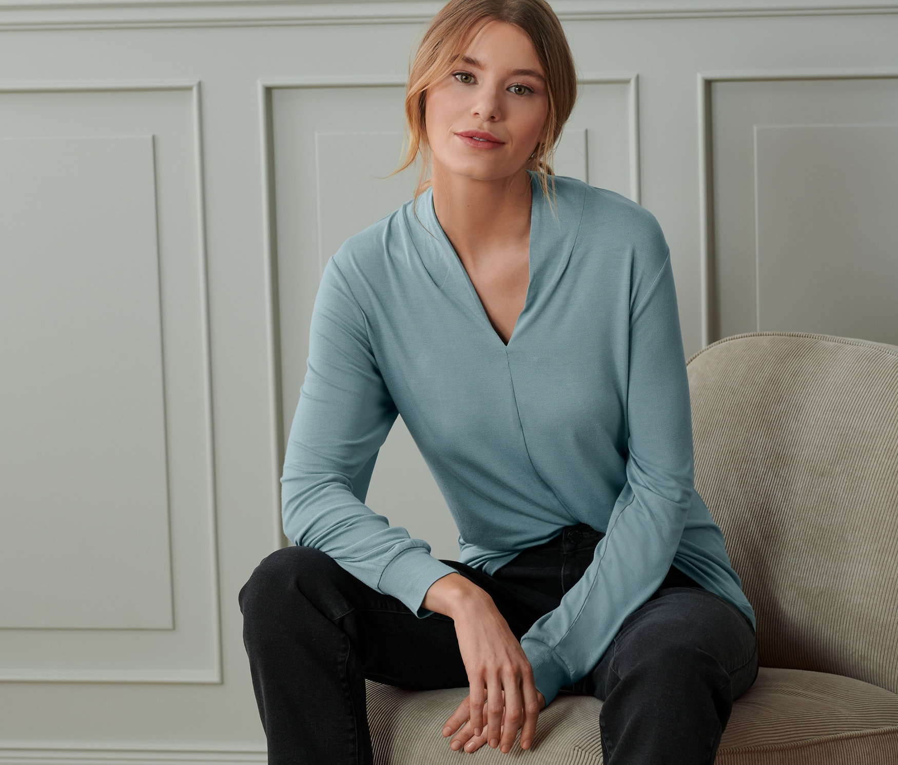 Žena sedí na židli a má na sobě kouřově modré triko s dlouhým rukávem a výstřihem do V.