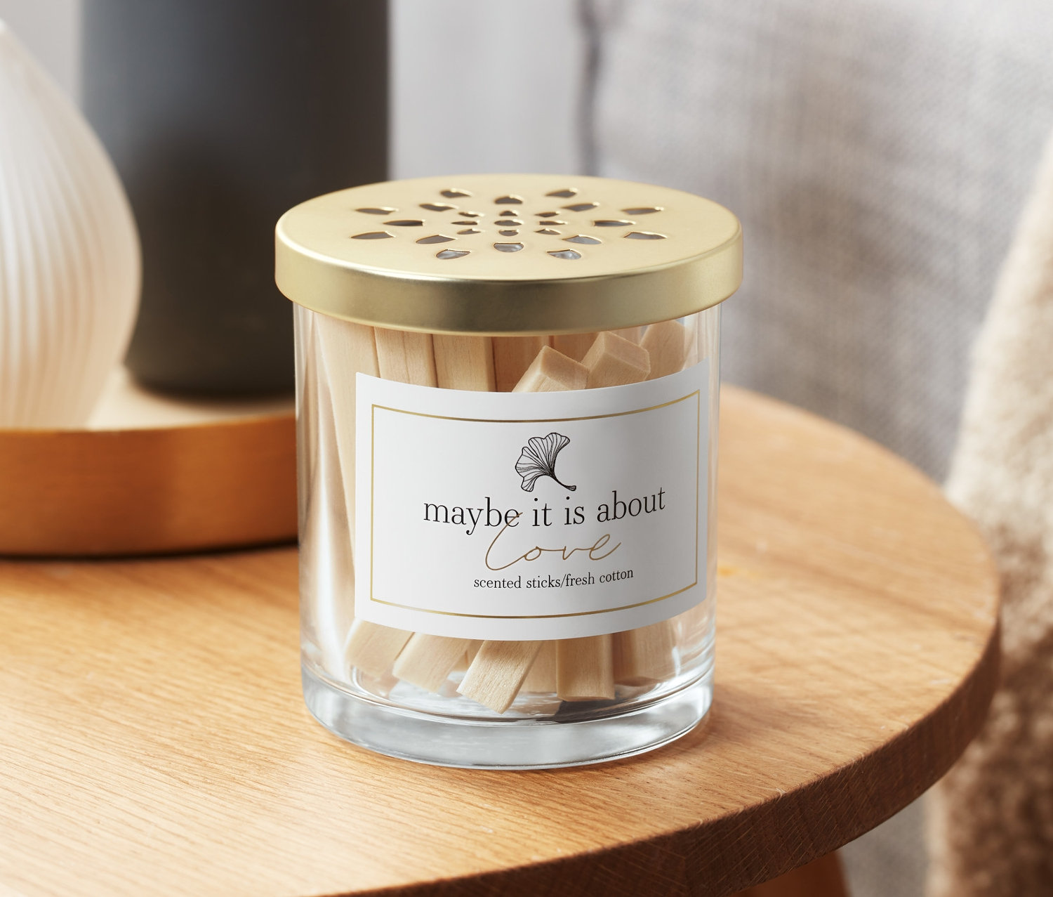 Skleněná nádoba s vonnými tyčinkami s vůní bavlněných polí na dřevěném stolku.