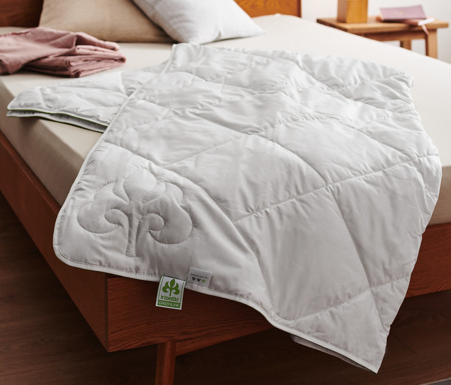 Na posteli leží bílá prošívaná přikrývka irisette® greenline z bavlny a lnu.