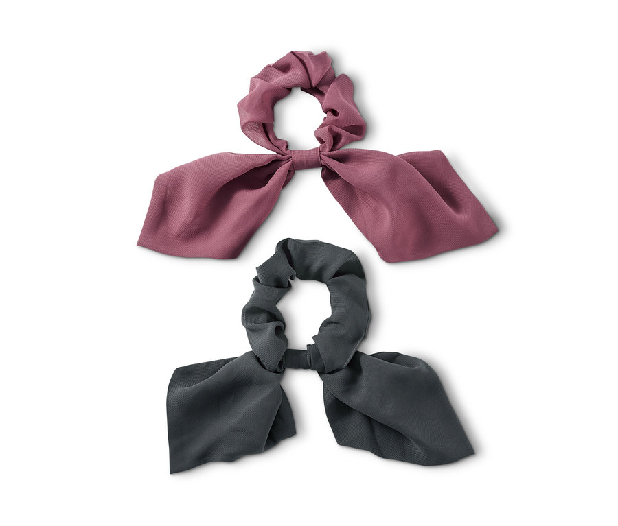 Dvě gumičky do vlasů »Scrunchies« s mašlí leží na bílém pozadí.