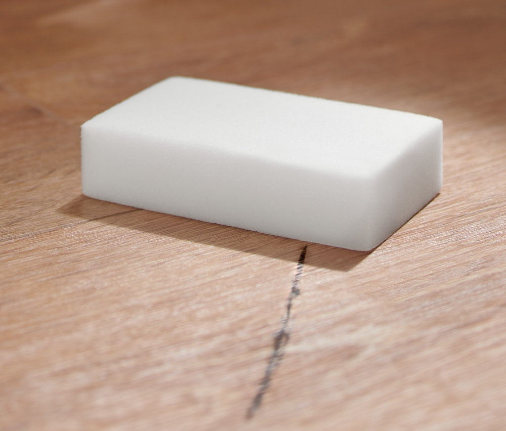 Čisticí houbička (10 ks) na dřevěné podlaze vedle béžového pufu.